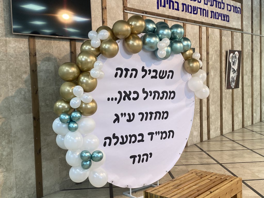 קשת בלונים בזהב, ירוק מטאלי ולבן סביב שלט עגול לטקס סיום בבית ספר