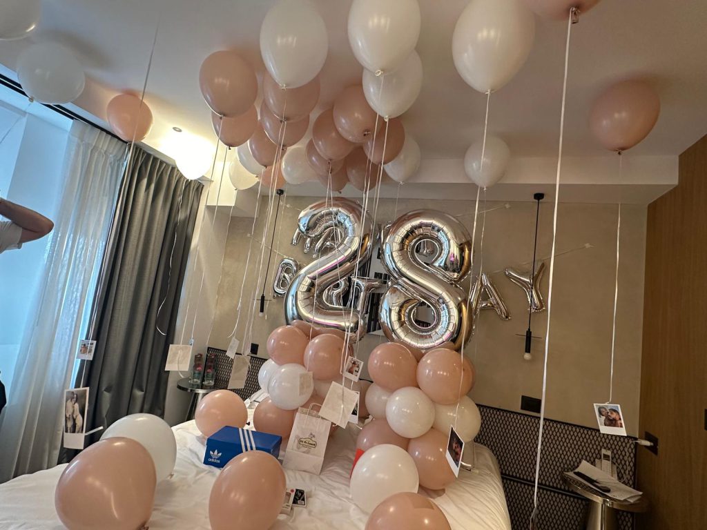 סידור בלונים לחדר מלון בגווני פודרה ולבן עם בלוני מספר 28 מכסף מעל המיטה