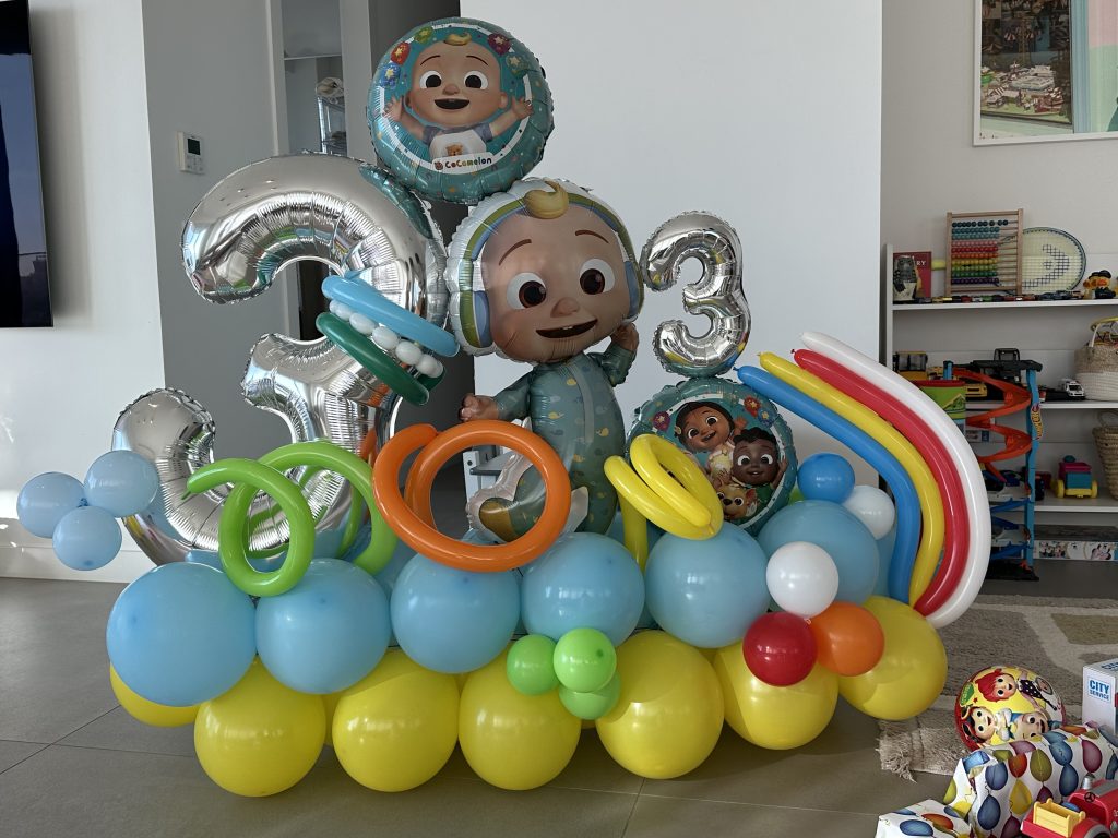 סטנד בלונים בעיצוב קוקומלון ליום הולדת, בלוני מספר מכסף על בסיס בלונים בצהוב, תכלת וירוק
