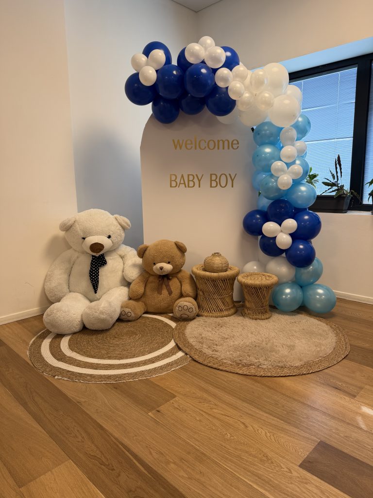מיצג בלונים בכחול, תכלת ולבן מול לוח welcome baby boy עם שני דובונים