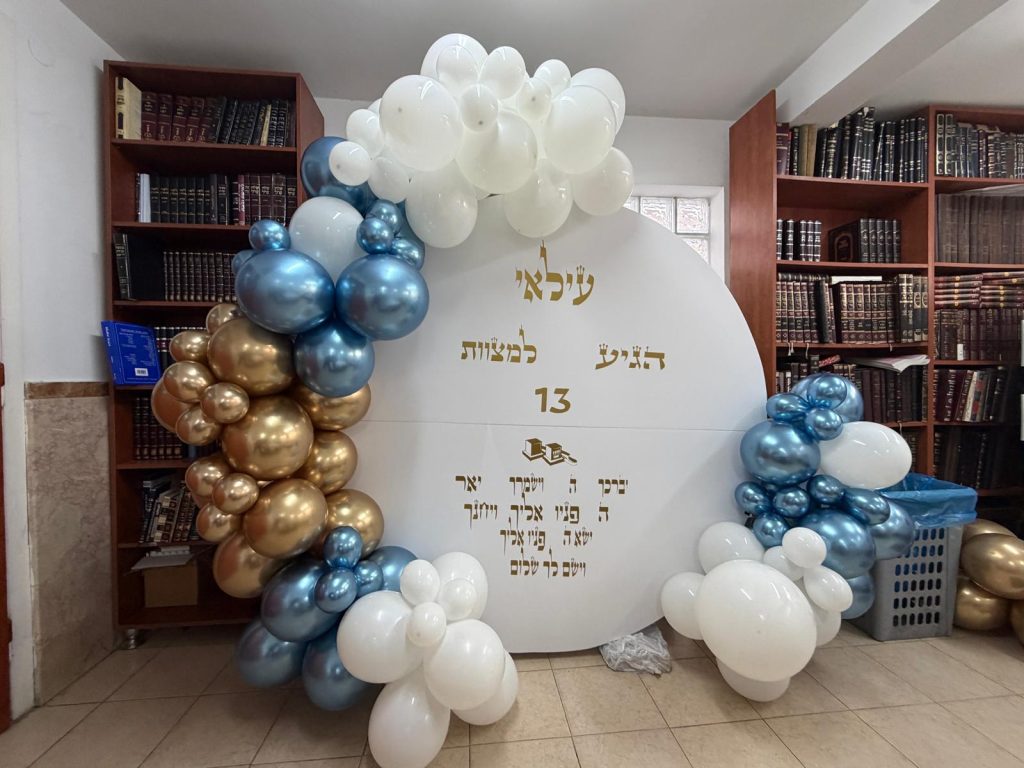 קשת בלונים בכחול, זהב ולבן סביב שלט עגול לבר מצווה