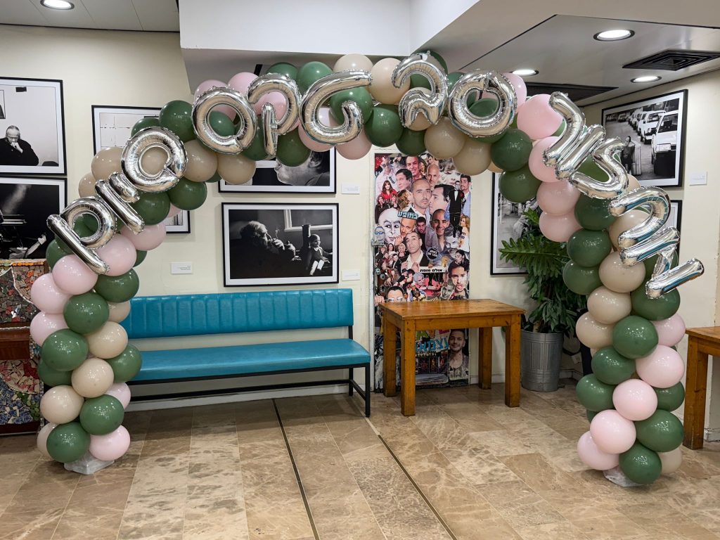 קשת בלונים בירוק, שמנת וכסף עם כיתוב בכניסה לאולם